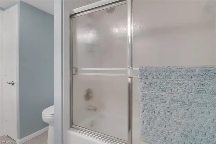 Full bath featuring combined bath / shower with glass door, toilet, and tile patterned floors