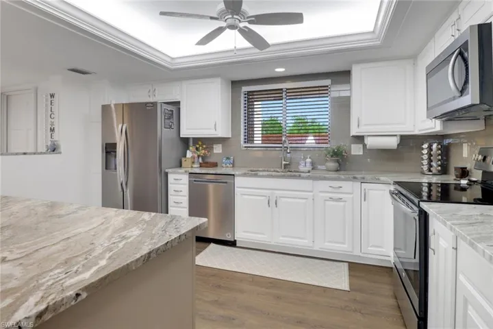 Kitchen with a sink, a tray ceiling, stainless steel appliances, and dark wood finished floors