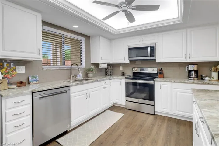 Kitchen featuring stainless steel appliances, a sink, white cabinetry, light wood finished floors, and a raised ceiling