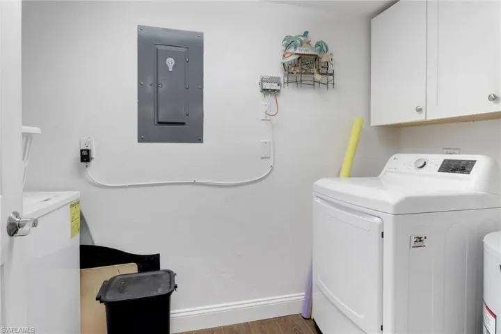 Laundry room with wood finished floors, baseboards, cabinet space, electric panel, and washer and clothes dryer