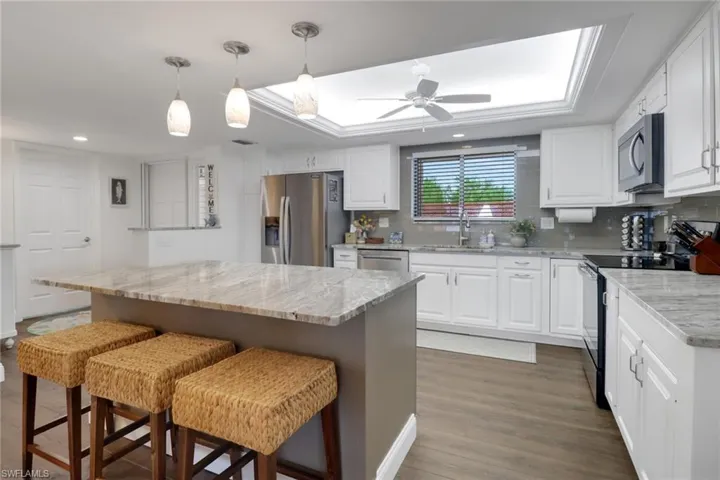 Kitchen with white cabinetry, appliances with stainless steel finishes, decorative backsplash, and a tray ceiling