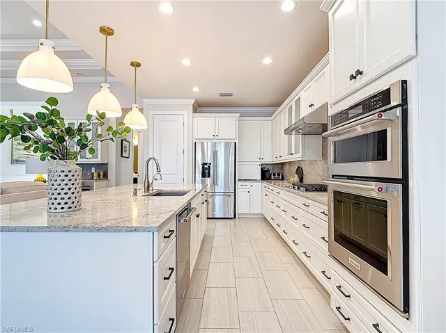Open kitchen with under cabinet lighting, stainless steel appliances, ornamental molding and custom backsplash