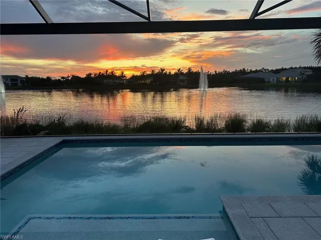 Pool at dusk with a water view, glass enclosure, and an outdoor pool