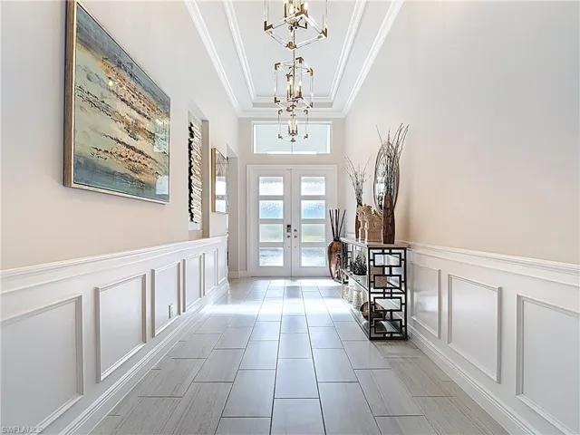 Entryway featuring crown molding, french doors, a notable chandelier, and a decorative wall