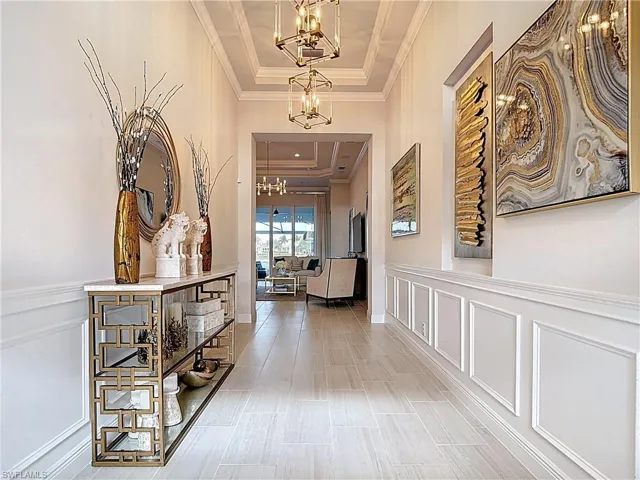 Entrance hallway featuring tray ceiling, wainscoted walls, ornamental moldings, and designer chandeliers
