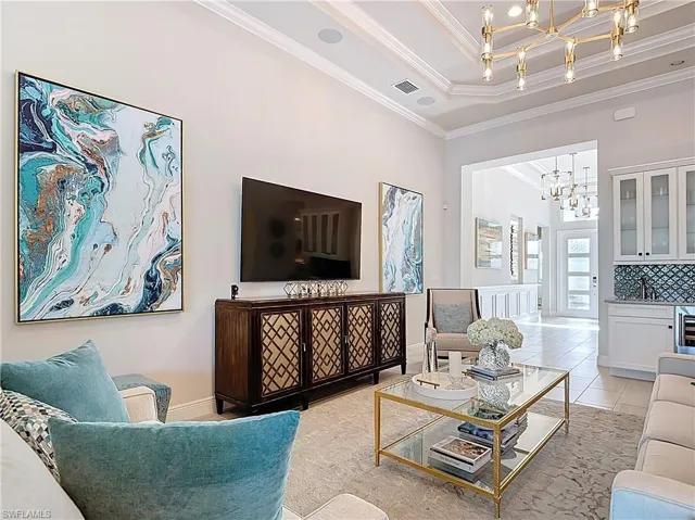 Living room with light tile patterned floors, a notable chandelier, ornamental molding, and coffered ceiling