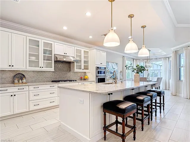 Kitchen with decorative backsplash, quartz countertops, enlarged center island, ornamental molding, stainless steel appliances, under cabinet range hood