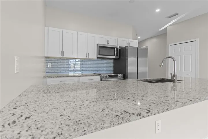 Kitchen with light stone countertops, white cabinetry, stainless steel appliances, and decorative backsplash