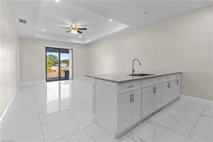 Kitchen featuring light stone countertops, a peninsula, a ceiling fan, light marble finish floors, and open floor plan