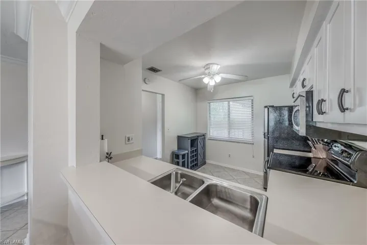 Kitchen with white cabinetry, appliances with stainless steel finishes, sink, ceiling fan, and light tile floors
