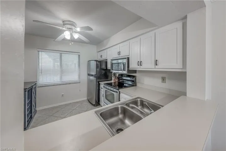 Kitchen with stainless steel appliances, white cabinets, sink, ceiling fan, and light tile floors