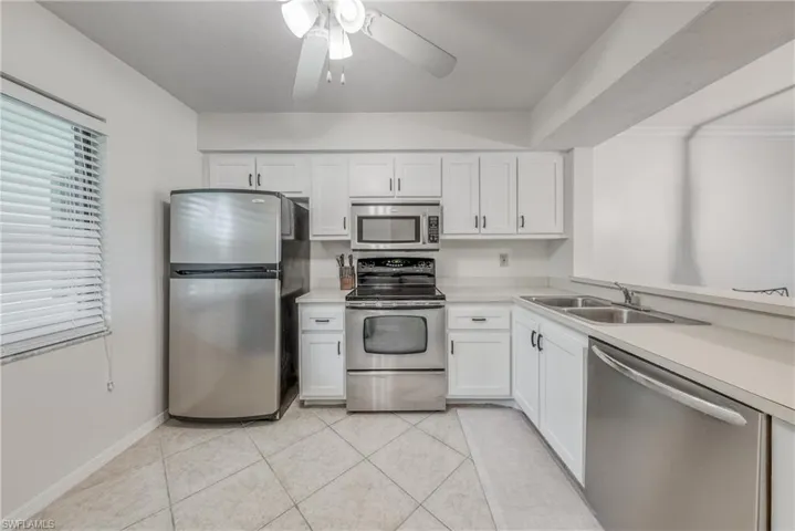 Kitchen featuring ceiling fan, stainless steel appliances, light tile floors, sink, and white cabinetry