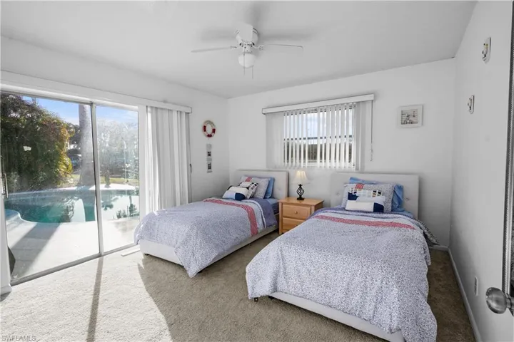 Guest bedroom #1 with patio doors to the pool, carpet, ceiling fan and window coverings.