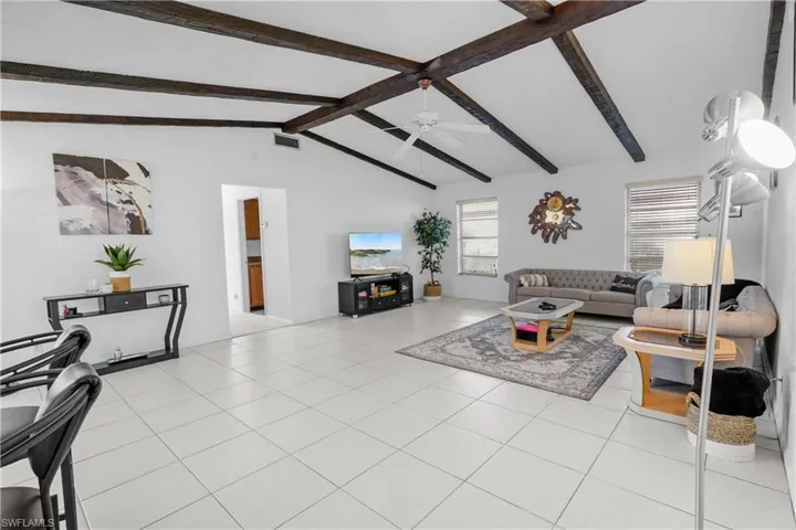 Living room with light colored large tile  large floors and high valuted ceiling and a celiling fan. Enterance to the guest wing and laundry room are off the family room.