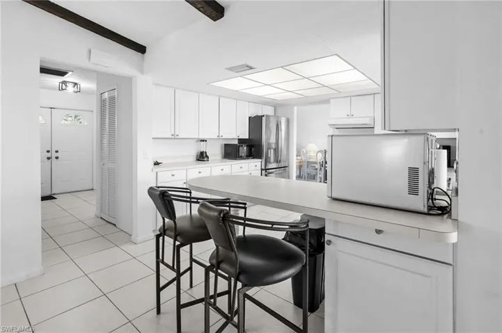 Kitchen featuring a kitchen bar, stainless steel appliances, white cabinetry, light countertops, and lofted ceiling with beams