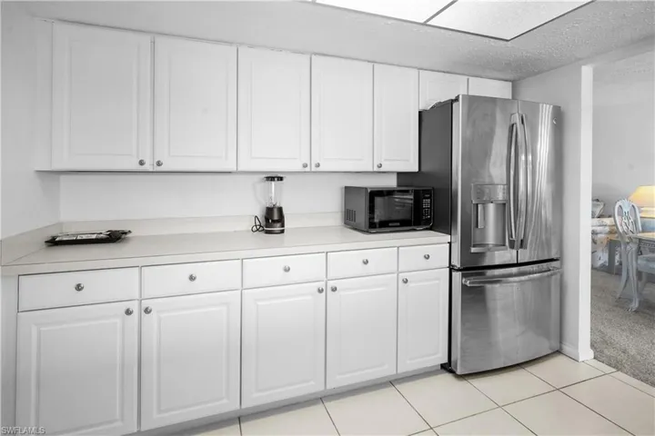 Kitchen with white cabinets, light countertops, stainless steel french door refrigerator with ice dispenser. Also nicely appointed with small appliances for a turnkey kitchen.