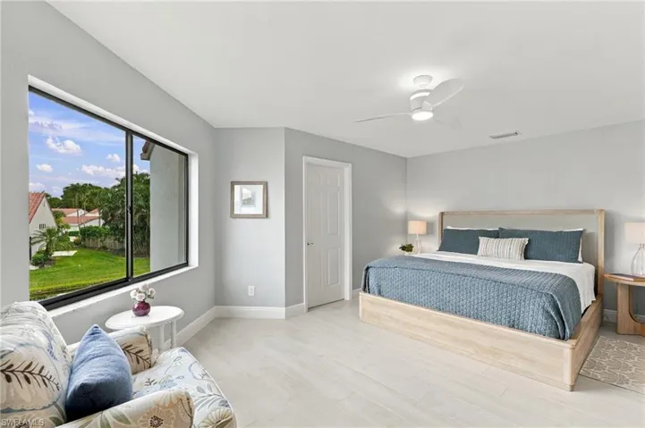 Large window providing natural light, light-toned wood-finish flooring, and a ceiling-mounted light fixture with integrated fan