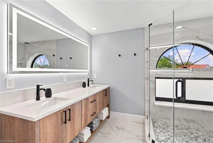 Double vanity with wood-finish cabinetry, quartz countertops, integrated LED-backlit mirror, and matte black hardware