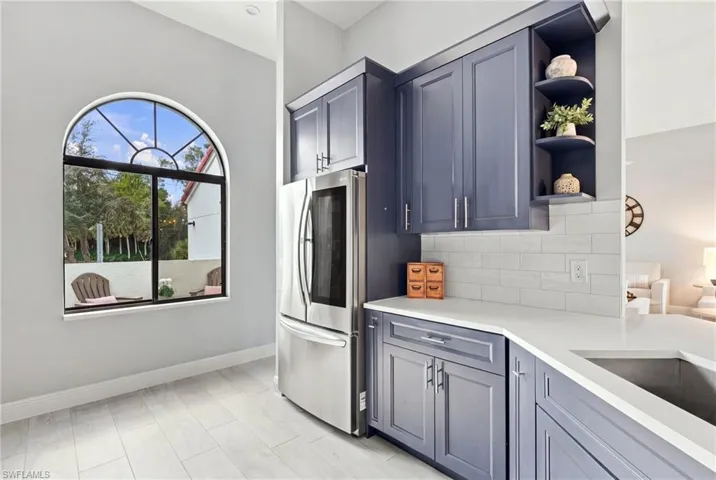 Kitchen featuring navy cabinetry, solid-surface countertops, subway tile backsplash, stainless steel refrigerator, and an arched window