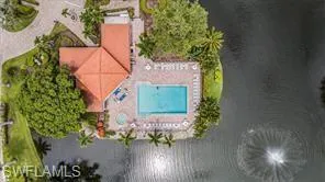 Aerial perspective of waterfront property featuring a tile roof, paved pool deck, swimming pool, integrated spa, and mature landscaping