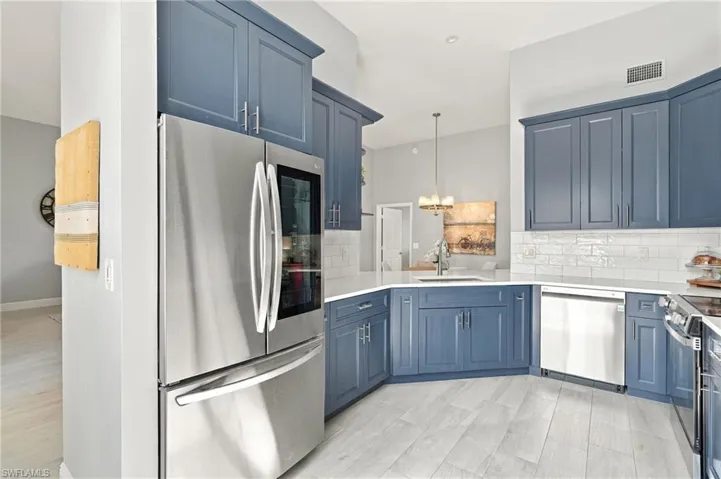 Blue cabinetry with satin nickel hardware, white stone countertops, subway tile backsplash, stainless steel appliances, and wood-finish flooring