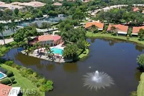 Aerial perspective featuring a community lake with a central fountain, an outdoor swimming pool, and tennis courts situated within a landscaped setting