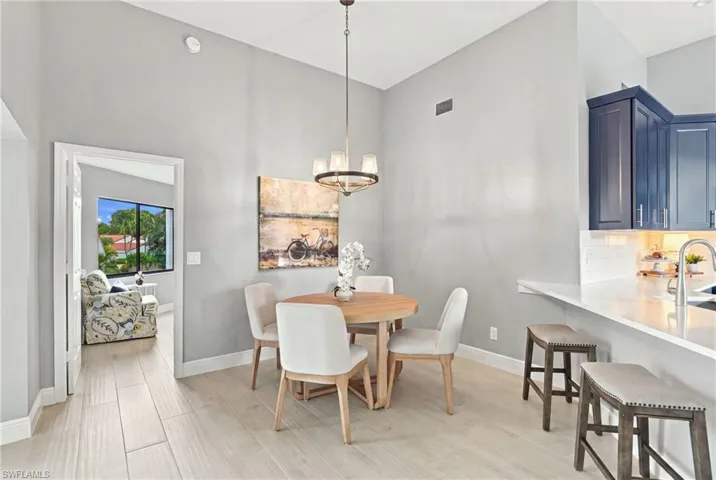 High-ceilinged dining area featuring wood-finish flooring, a contemporary chandelier, custom navy blue cabinetry, and white countertops