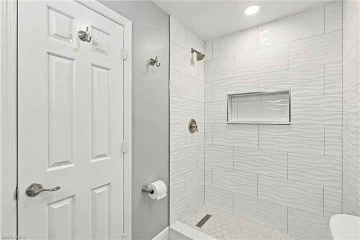 Walk-in shower featuring white wave-textured wall tile, hexagonal floor tile, recessed shelving, and a metallic shower fixture