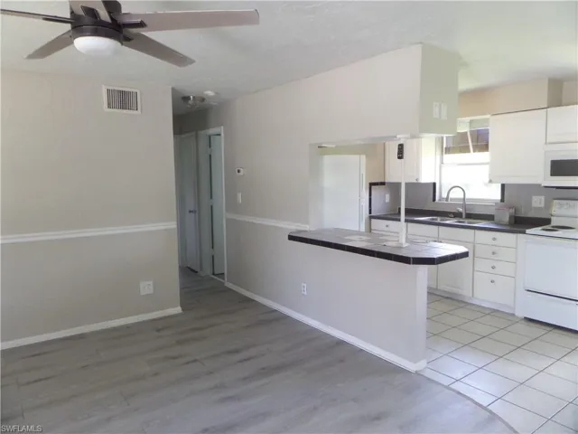 Kitchen with white appliances, tile counters, white cabinetry, and ceiling fan