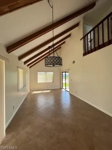 Unfurnished living room featuring high vaulted ceiling, dark tile patterned floors, and beam ceiling