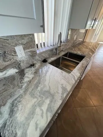 Details featuring dark tile patterned flooring, light stone counters, sink, and backsplash