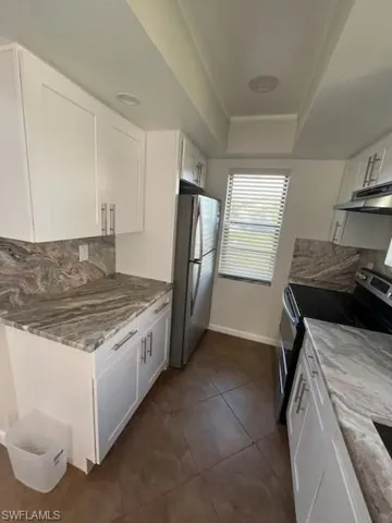 Kitchen with dark tile patterned floors, range, tasteful backsplash, stainless steel refrigerator, and white cabinets