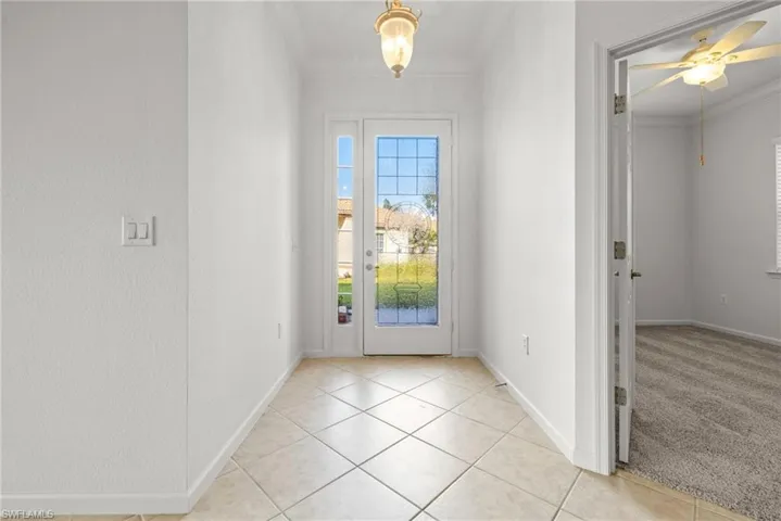 Doorway to outside featuring crown molding, ceiling fan, and light tile patterned floors