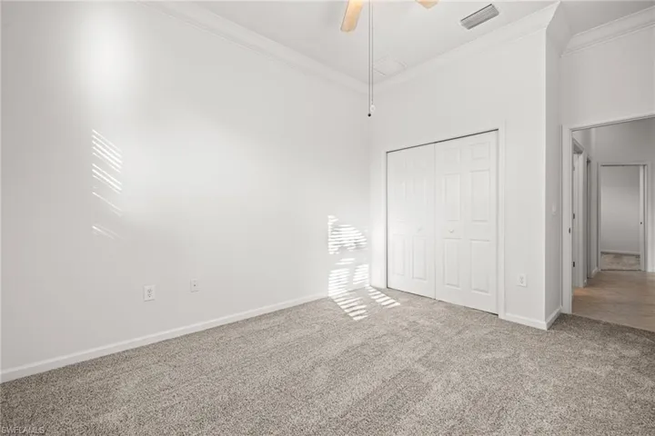 Unfurnished bedroom with ceiling fan, a towering ceiling, carpet flooring, ornamental molding, and a closet