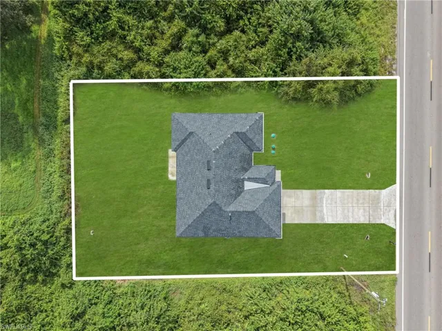 Aerial perspective showcasing a property with a distinct roofline, expansive green lawn, and concrete driveway