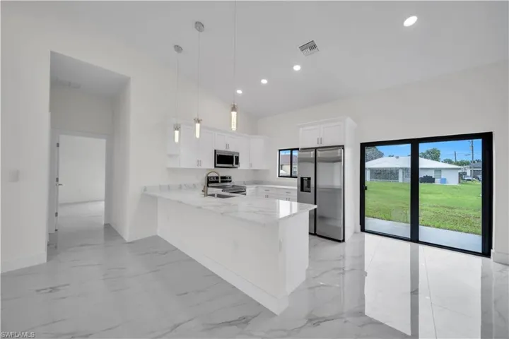 Modern kitchen featuring white cabinetry, a large island with a surface, stainless steel appliances, and sliding glass doors