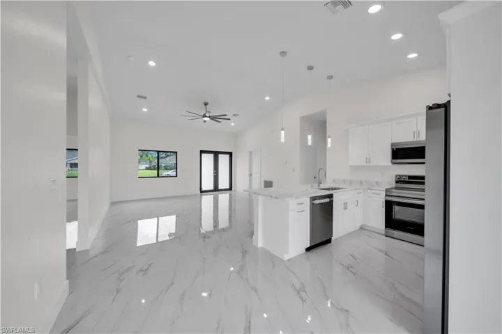 Kitchen with stainless steel appliances and white cabinetry, featuring a central island with a sink and pendant lighting