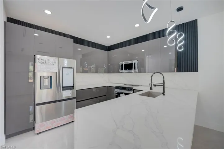 Kitchen with stainless steel appliances, modern cabinets, light stone counters, decorative light fixtures, and a peninsula