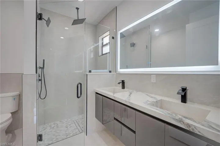 Bathroom featuring a shower stall, double vanity, and tile walls