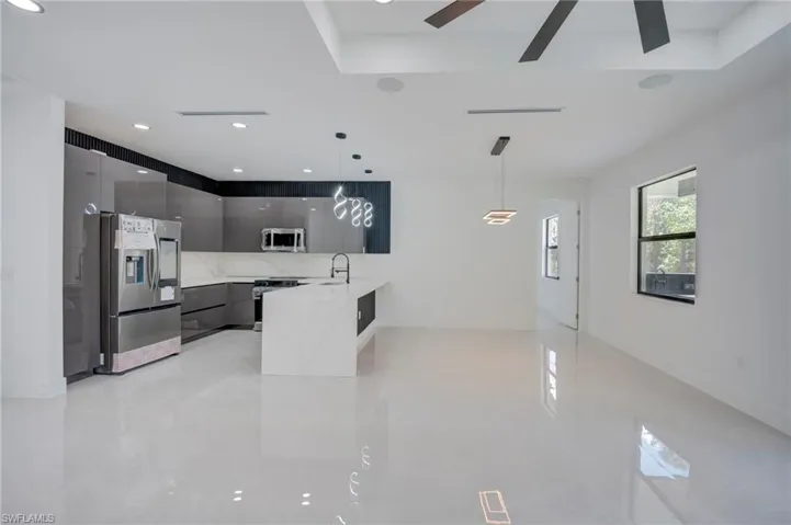 Kitchen with modern cabinets, stainless steel fridge, stove, pendant lighting, and light stone counters