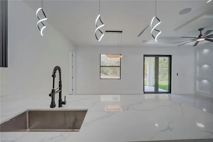 Kitchen featuring light stone countertops, open floor plan, a ceiling fan, french doors, and hanging light fixtures