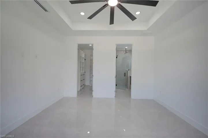 Unfurnished bedroom featuring a tray ceiling, a walk in closet, recessed lighting, ceiling fan, and ensuite bath