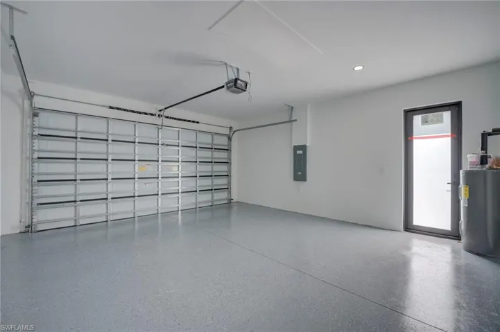 Garage featuring electric water heater, electric panel, recessed lighting, and a garage door opener