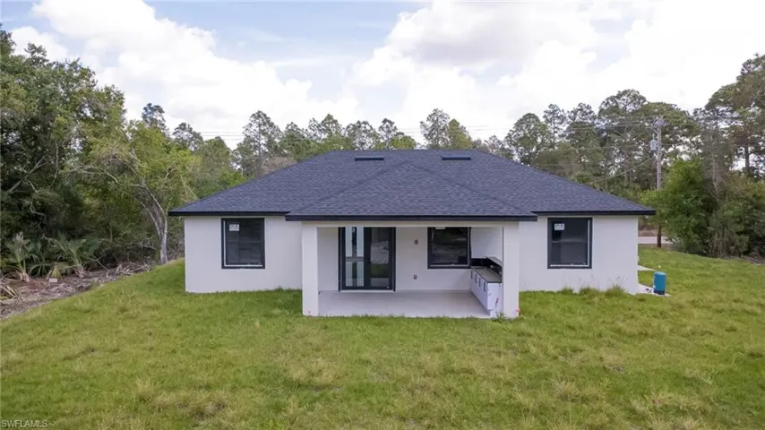 Rear view of property featuring a shingled roof, a lawn, stucco siding, and a patio area