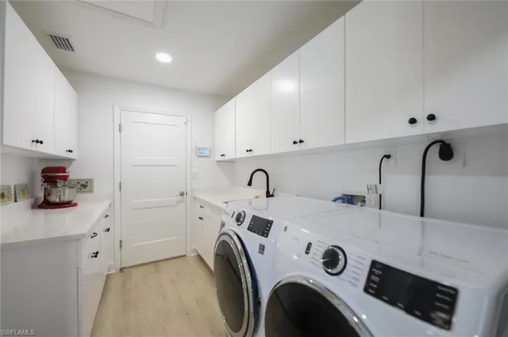 Laundry area featuring crisp white cabinetry, light-toned countertop surfaces, wood-finish flooring, a matte black faucet, and overhead recessed lighting