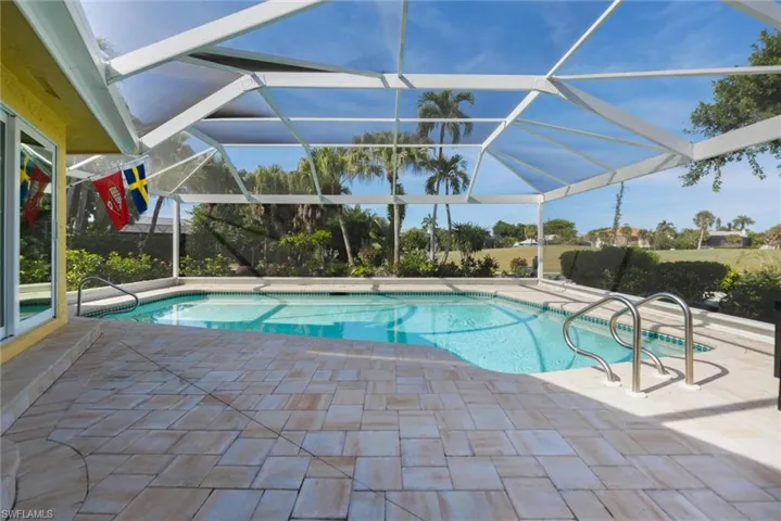 Screen-enclosed swimming pool featuring a built-in step entry, stone-paver decking, and metal handrails