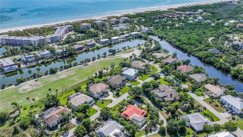 Aerial perspective of a coastal residential community featuring waterfront property, dense native landscaping, proximity to the shoreline, and paved street infrastructure