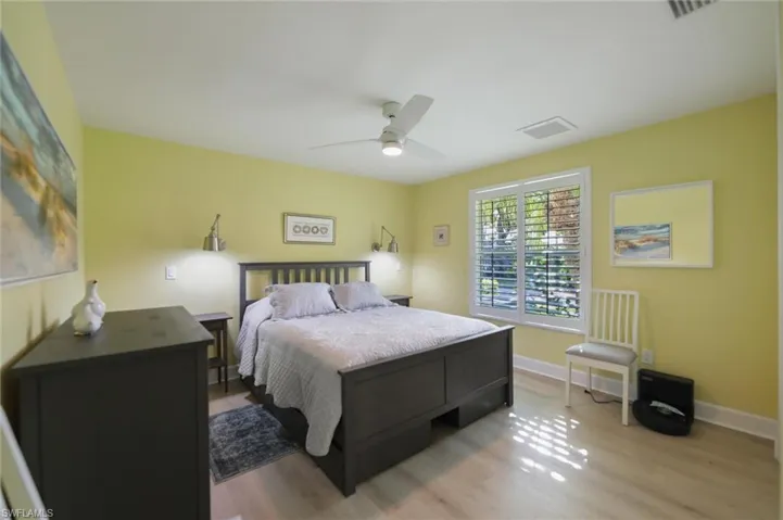 Bedroom featuring wood-finish flooring, plantation shutters, a ceiling fan with integrated lighting, and dual wall-mounted reading sconces
