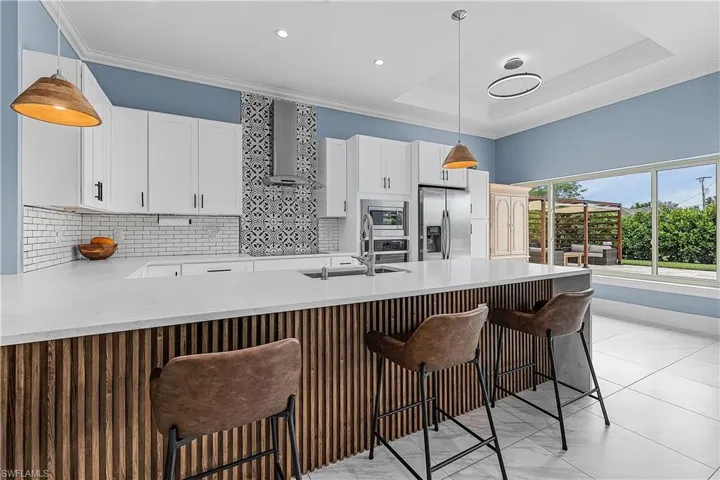 Kitchen with light stone counters, white cabinetry, decorative backsplash, a peninsula, and a breakfast bar area