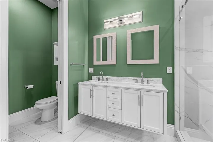 Primary bathroom featuring double vanity, light floors, and a marble finish shower